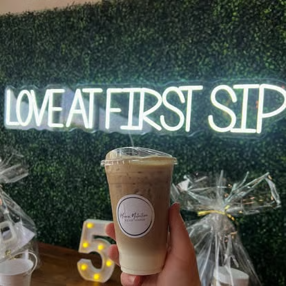 A Monroe Nutrition drink held up in front of a neon sign reading Love at First Sip